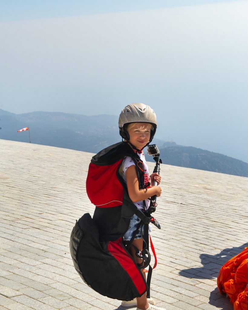 a-little-girl-in-paragliding-gear-and-with-a-camera-stands-on-the-edge-of-mount-babadag-turkey-1.jpg